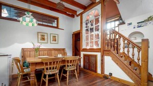 A dining area with a wooden table and chairs, a hanging light fixture, and a staircase with wooden railings. - Park Mill Cottages | The Granary (St Andrews)