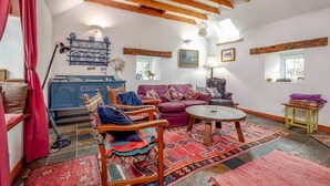 A cozy living room with a wooden ceiling, a blue cabinet, a purple sofa, and a round coffee table. - Park Mill Cottages | The Granary (St Andrews)