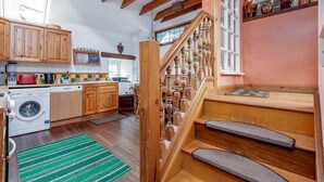 A kitchen with wooden cabinets, a washing machine, and a staircase with a wooden railing. - Park Mill Cottages | The Granary (St Andrews)