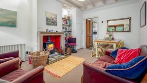 A cozy living room with a fireplace, leather sofas, a bookshelf, and a dining area. - Park Mill Cottages | Mill Cottage (St Andrews)