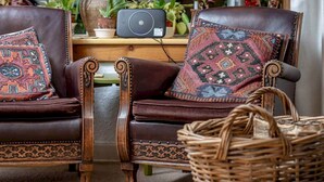 Two brown leather chairs with patterned cushions, a wicker basket, and a black speaker on a wooden table. - Park Mill Cottages | Mill Cottage (St Andrews)