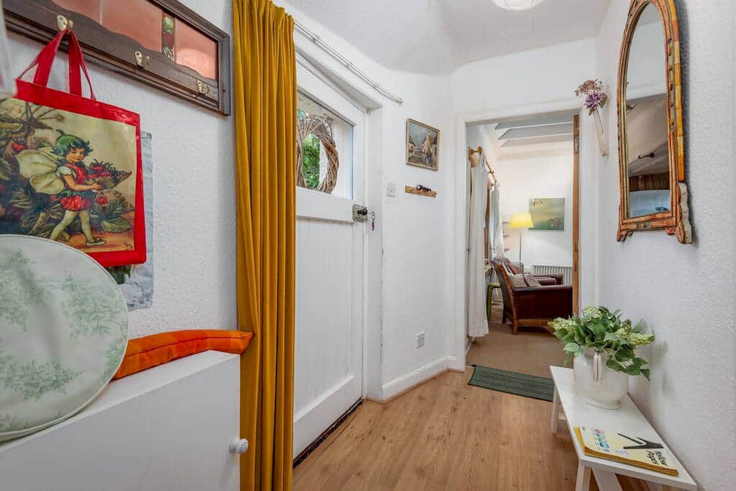 A hallway with a wooden floor, a yellow curtain, a red bag, a framed picture, and a mirror on the wall.