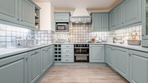 A kitchen with light blue cabinets, a microwave, an oven, and a tiled backsplash. - Crail Town House (Crail)
