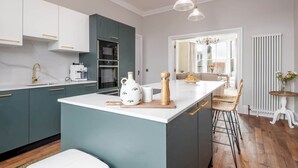 A modern kitchen with a central island, white cabinets, and a view into the dining area. - Skye Sands | Alexandra Penthouse (No 11) (St Andrews)