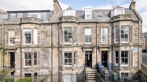 A historic stone building with multiple windows and a prominent corner turret. - Skye Sands | Alexandra Penthouse (No 11) (St Andrews)