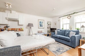Un salon moderne comprenant un lit, un canapé, un téléviseur et un coin cuisine avec des placards et une cuisinière.