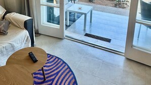 Et hotelværelse med en seng, et lille bord og udsigt til et stykke klippelandskab og vand gennem en åben dør.