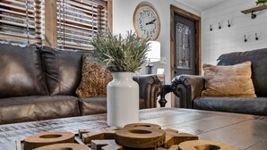 A living room with a brown leather sofa, a white vase with green plants, and a wooden coffee table with geometric wooden pieces. - Secluded cabin close to Eureka Springs and Table Rock Lake (Eureka Springs)