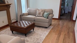 A living room with a beige sofa, a brown ottoman, and a patterned rug. - The Mint Julep - Charming Cottage in Historic Fayetteville - near Round Top (Fayetteville)