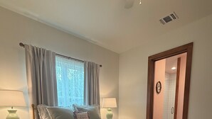 A bedroom with a bed, two bedside tables, a window with curtains, a door, and a ceiling fan. - The Mint Julep - Charming Cottage in Historic Fayetteville - near Round Top (Fayetteville)