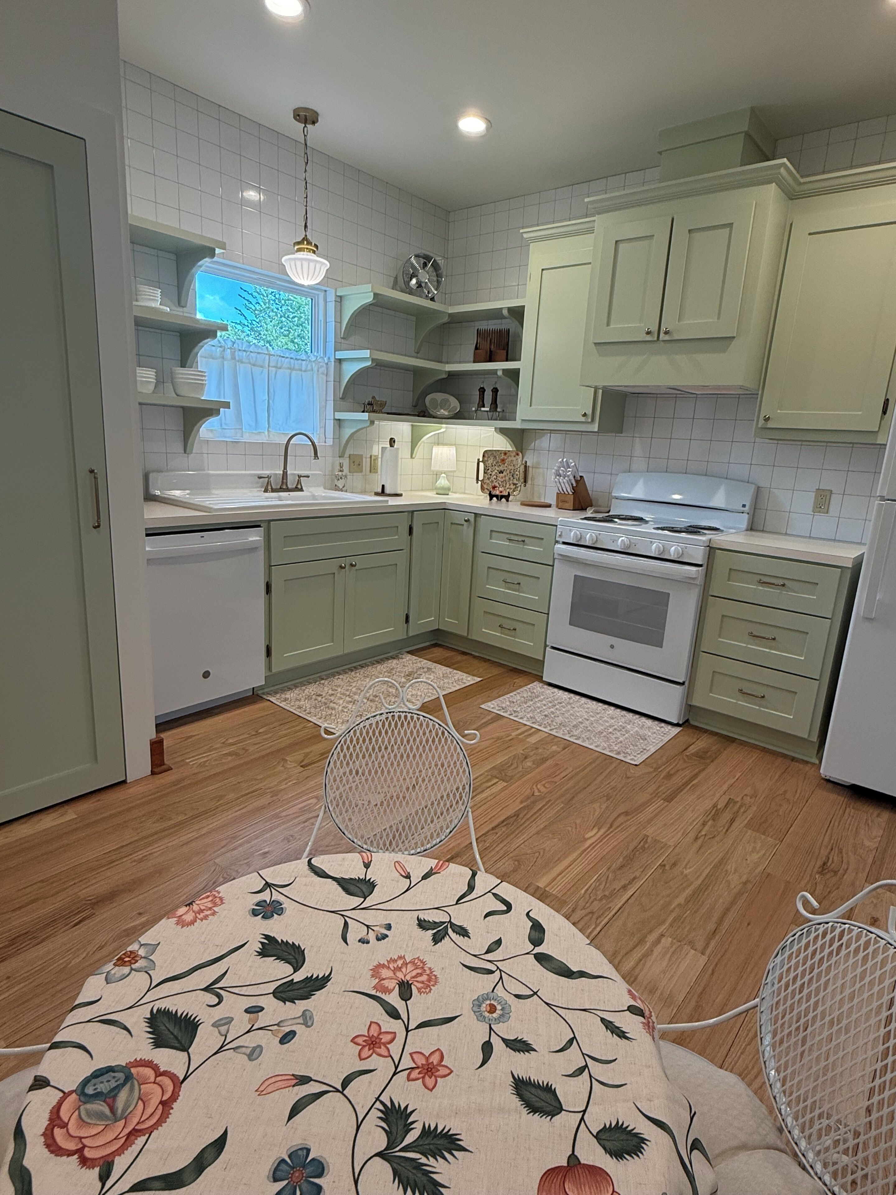 A modern kitchen with light green cabinets, a white stove, and a dining area with a floral tablecloth.