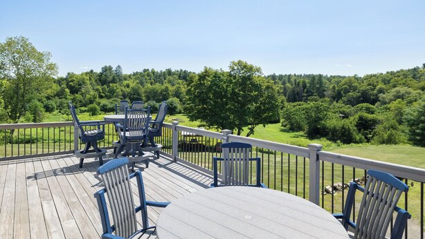 Eine Holzterrasse mit Gartenmöbeln, einem Geländer und Blick auf eine grüne Landschaft.