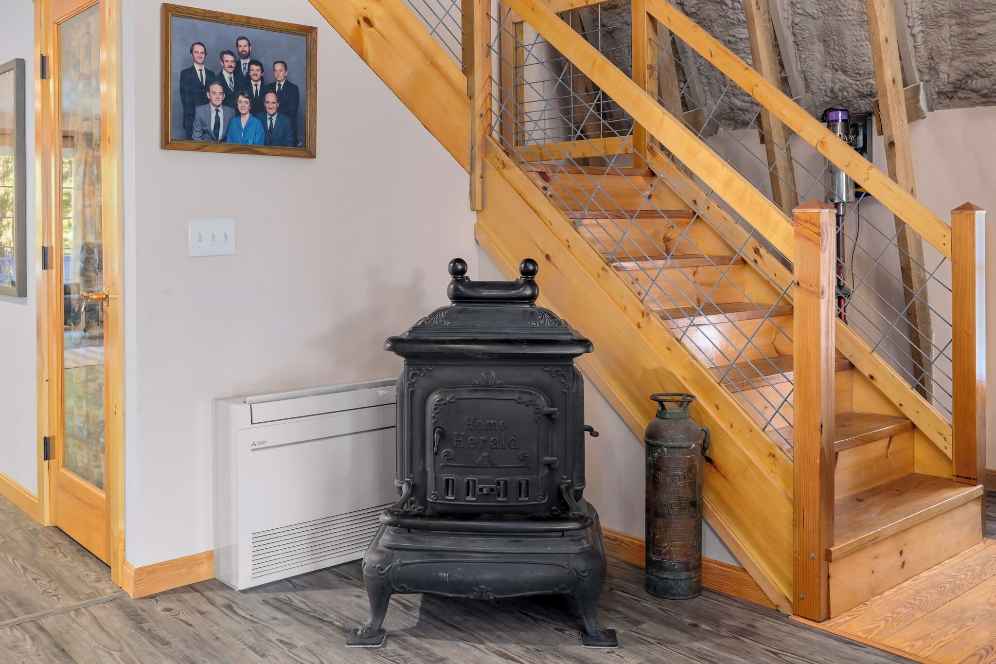 Ein Zimmer mit einer Holztreppe, einem alten Herd, einem gerahmten Foto an der Wand und einem Feuerlöscher.