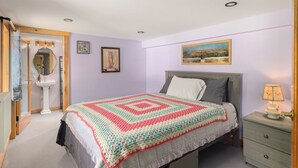 Ein Schlafzimmer mit einem Bett, einem Nachttisch, einer Lampe, einem gerahmten Bild und einem Spiegel.