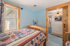 Un dormitorio con cama, ventana, puerta y pasillo.