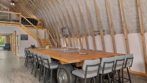 Ein Essbereich mit einem großen Holztisch und grauen Stühlen, einer Treppe und Blick ins Freie.