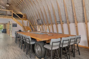 Un comedor con una amplia mesa de madera y sillas grises, una escalera y vistas al exterior.