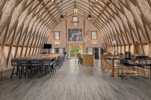 Ein geräumiger Raum mit einer hohen, gewölbten Decke, einem langen Tisch mit Stühlen und einer Küchenzeile inklusive Kühlschrank und Herd.