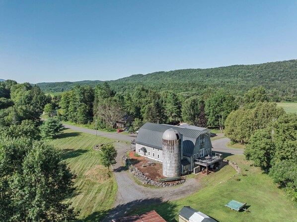Ein großes Bauernhaus mit einem Silo, umgeben von üppigem Grün und blauem Himmel.
