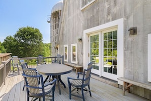 A deck with a round table and chairs, a large window, and a water tank.