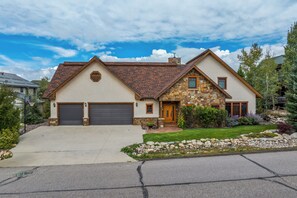 A two-story house with a stone facade, a garage, and a well-maintained lawn. - Walk to Downtown! Hot Tub! Garage Parking! (Steamboat Springs)