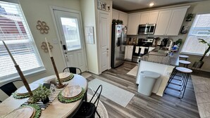 Een moderne keuken met witte kasten, roestvrijstalen apparatuur en een eethoek met een ronde tafel en stoelen.