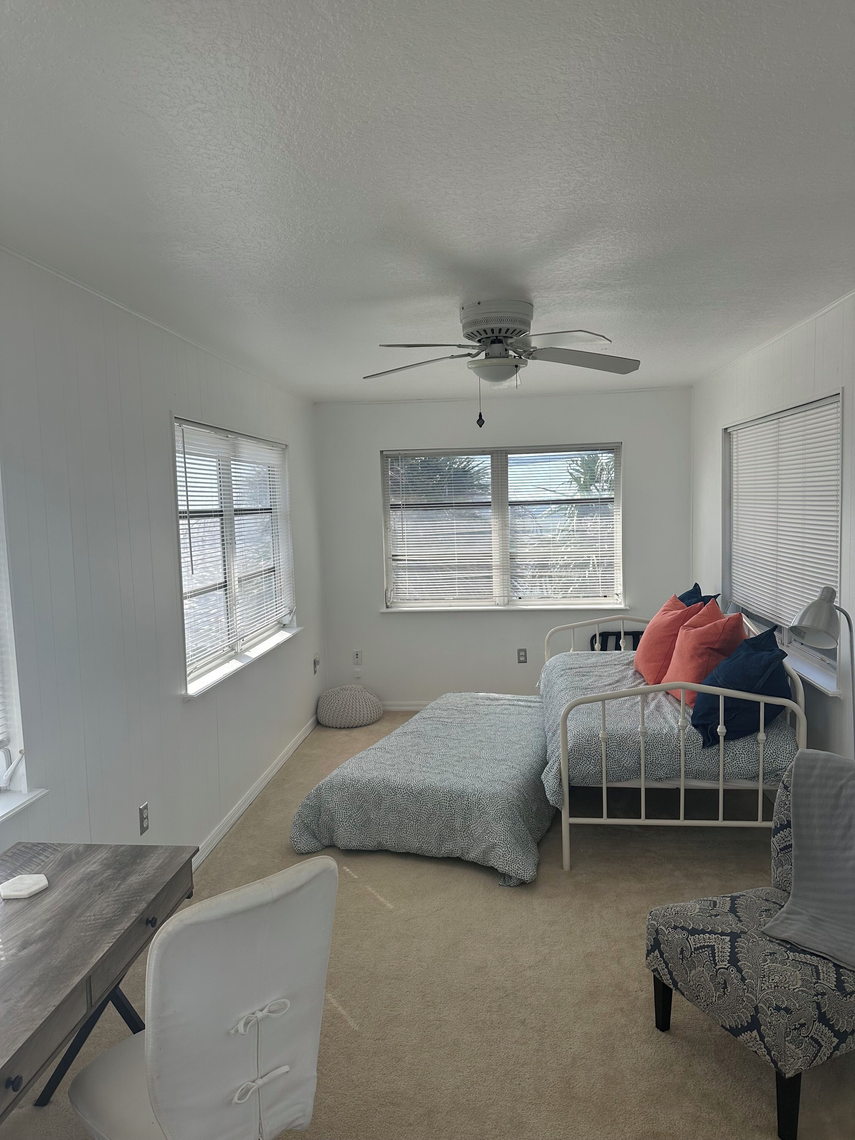 A bedroom with a bed, a desk, a chair, and a ceiling fan.