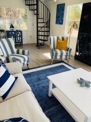 Una sala de estar con sillones a rayas, una mesa de centro blanca y una alfombra azul.