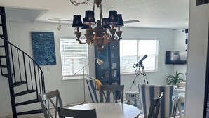 Uma sala de jantar com uma mesa redonda, cadeiras escuras, um lustre e uma escada.