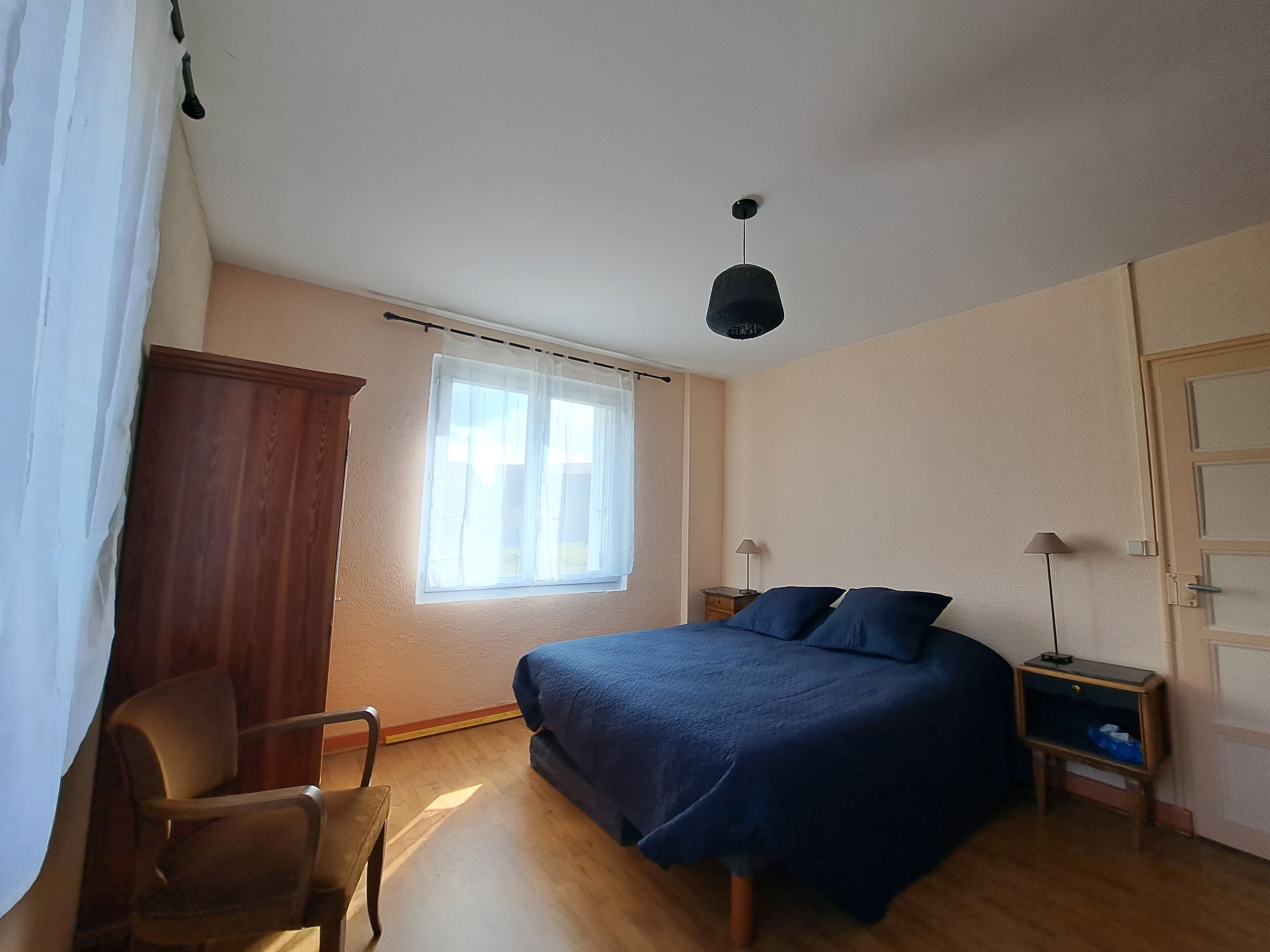A bedroom with a bed, a chair, a nightstand, a lamp, and a window with curtains.