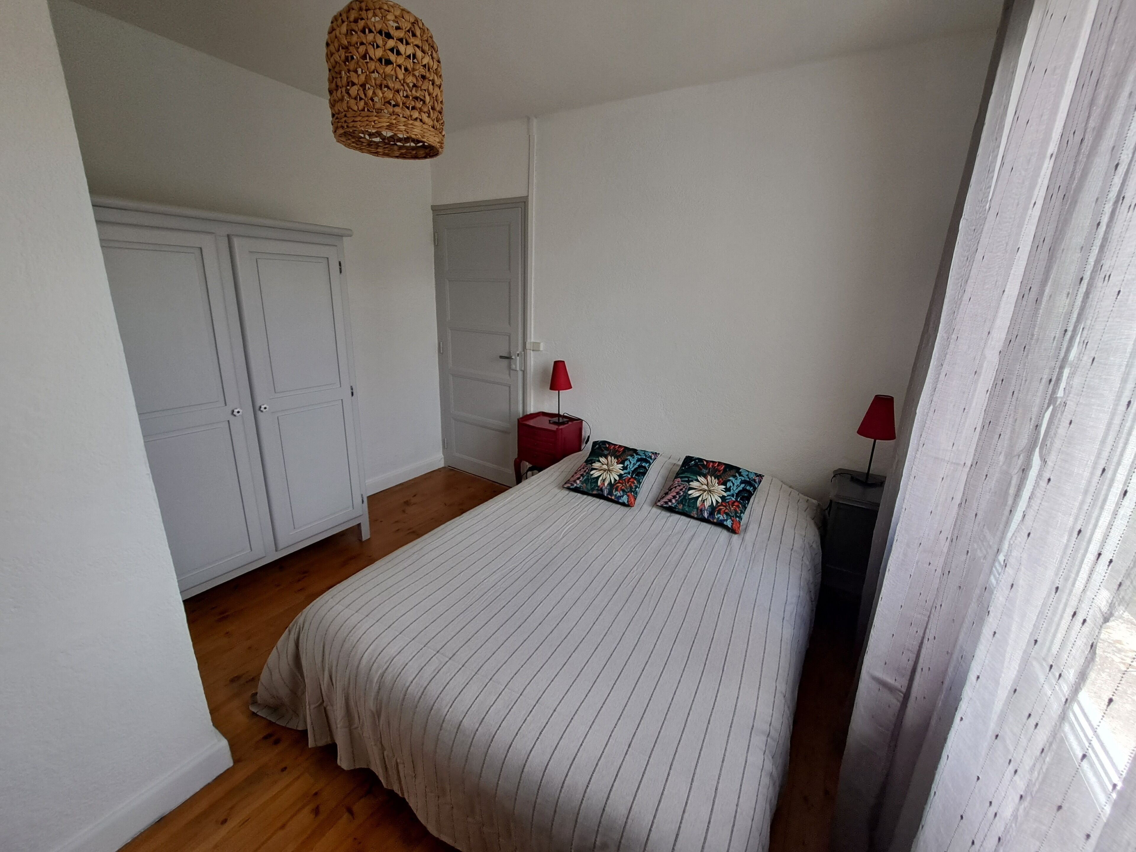 Een slaapkamer met een groot bed, twee nachtkastjes, een hanglamp en een kledingkast.