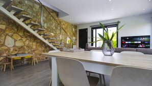 A modern kitchen with a stone wall, a wooden dining table, and a staircase leading to an upper level. - Villa CLANXET (Cambrils)