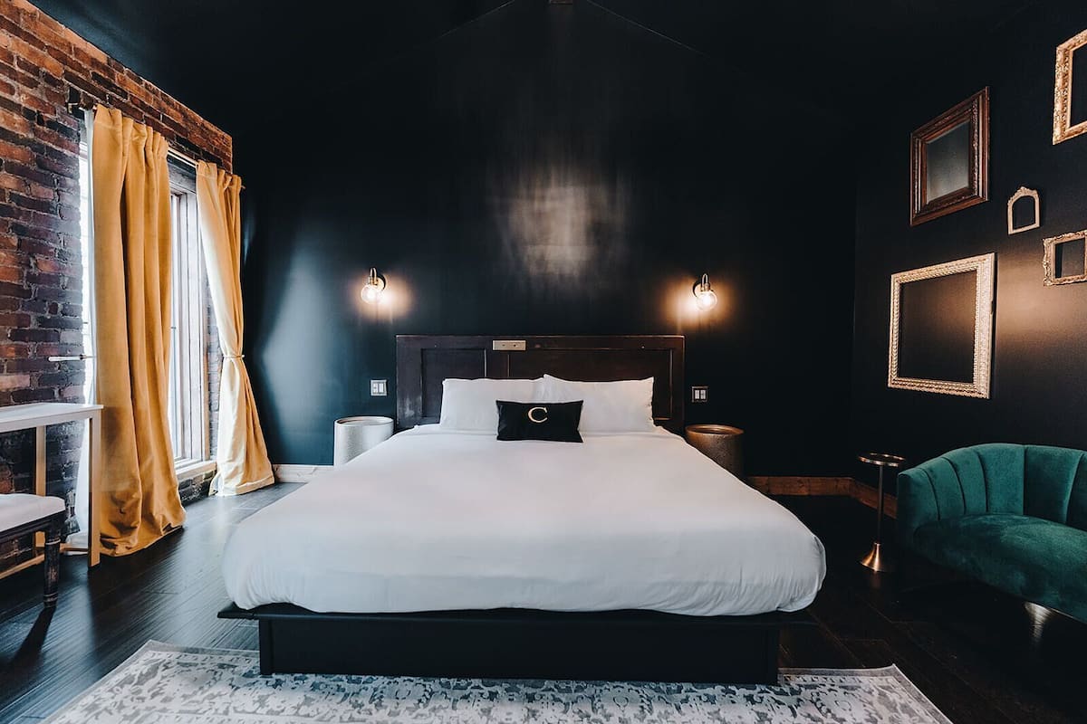 A modern bedroom with a large bed, a brick wall, and a green armchair.