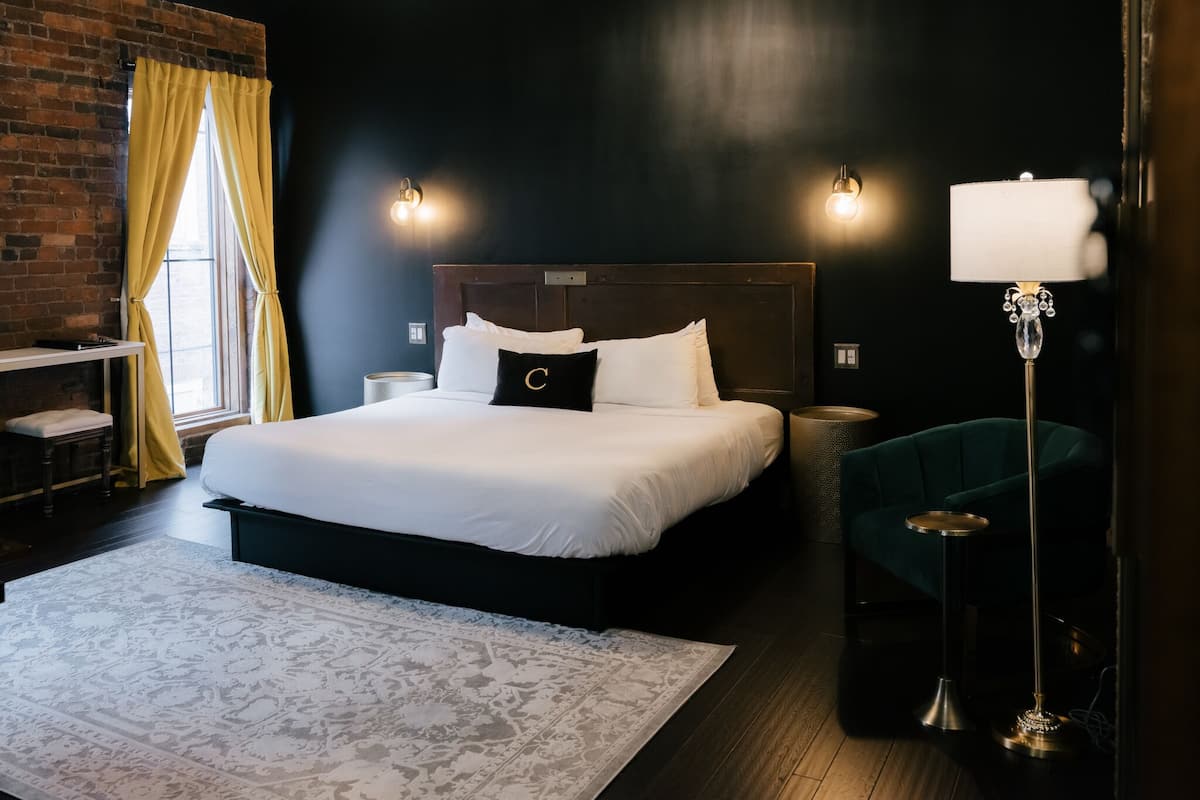 A modern hotel room with a large bed, a desk, a chair, and a floor lamp.
