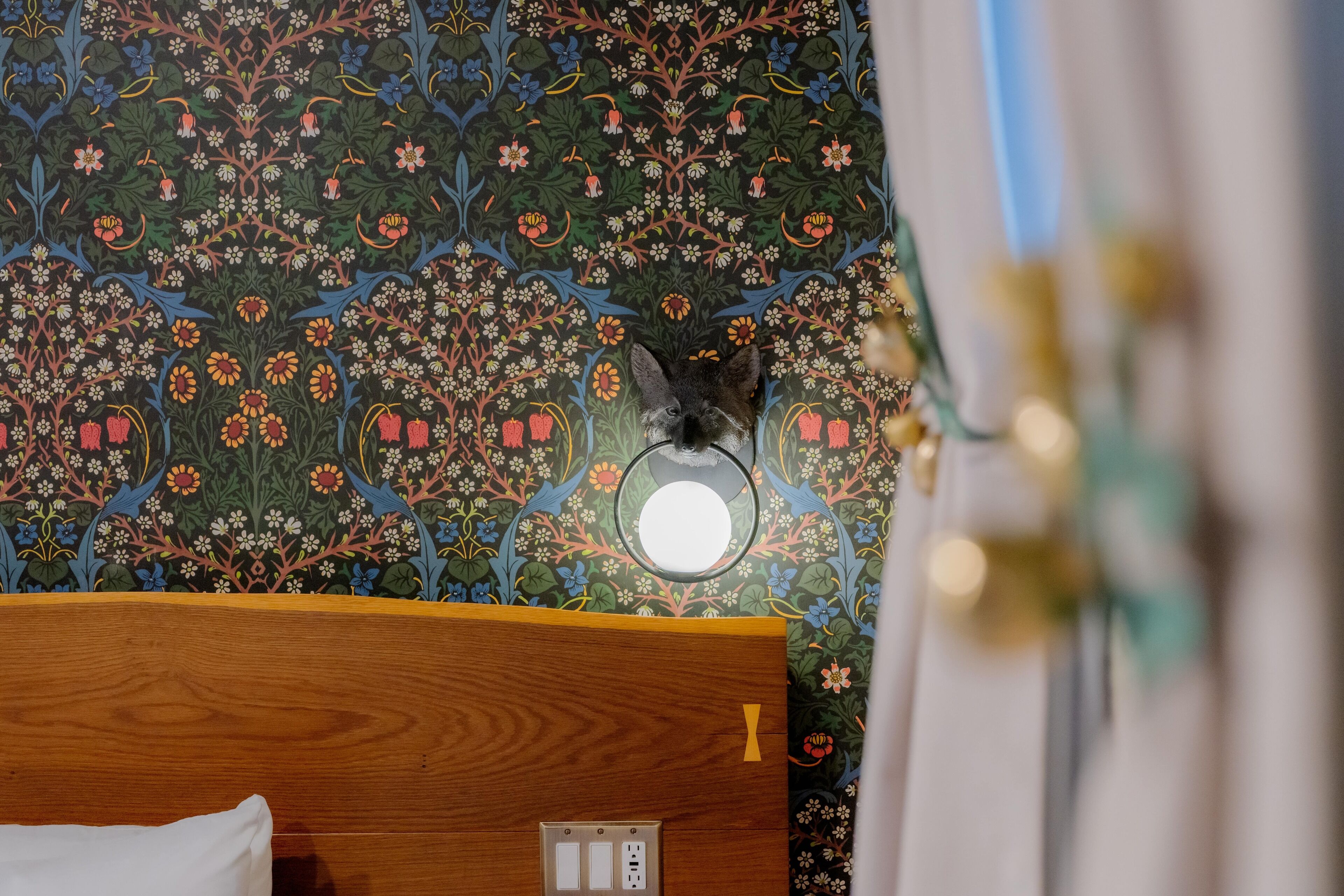 Una habitación con papel tapiz floral, cabecero de madera y un espejo redondo en la pared.