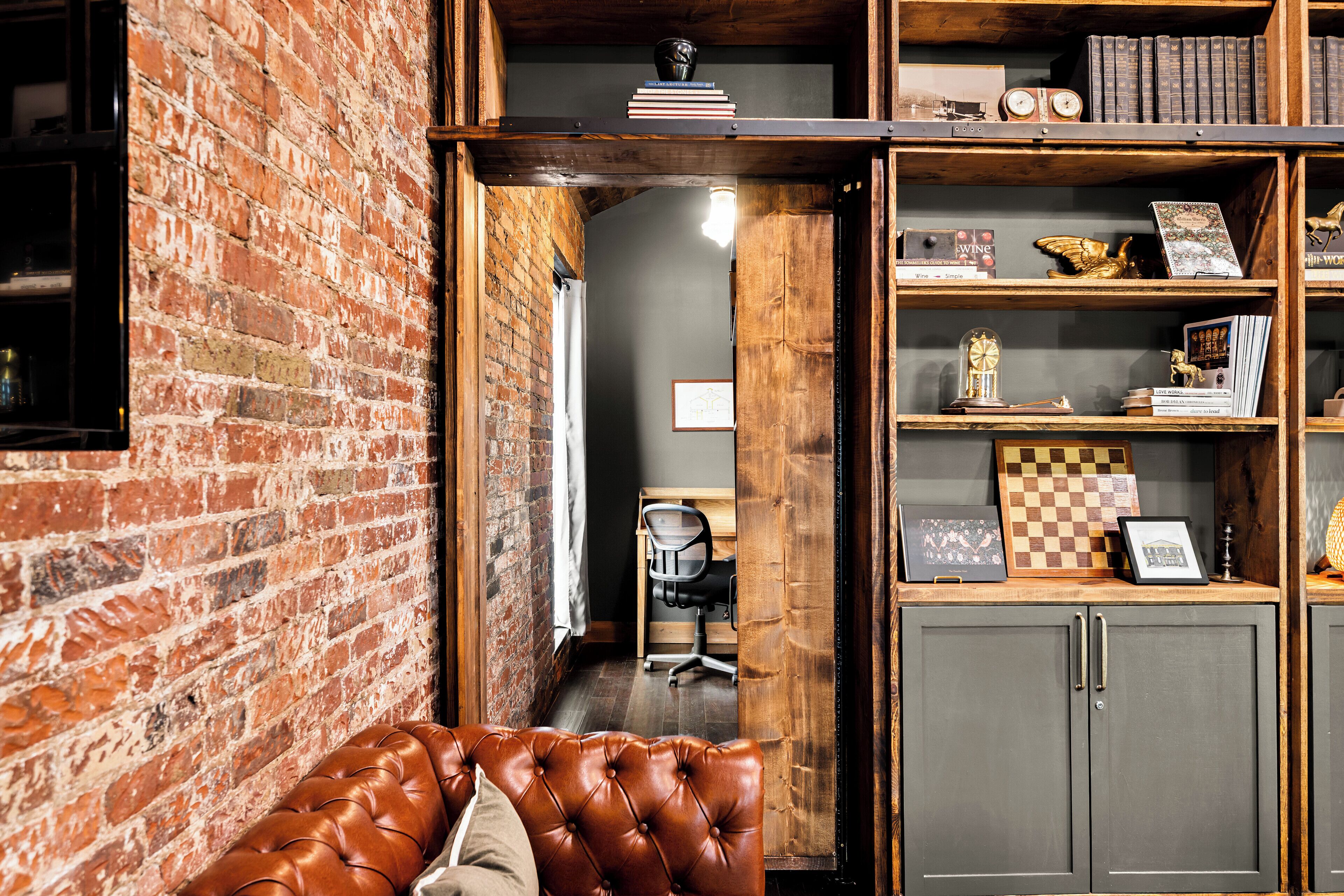 Una habitación con pared de ladrillo, sofá de cuero y estantería de madera con libros y objetos decorativos.