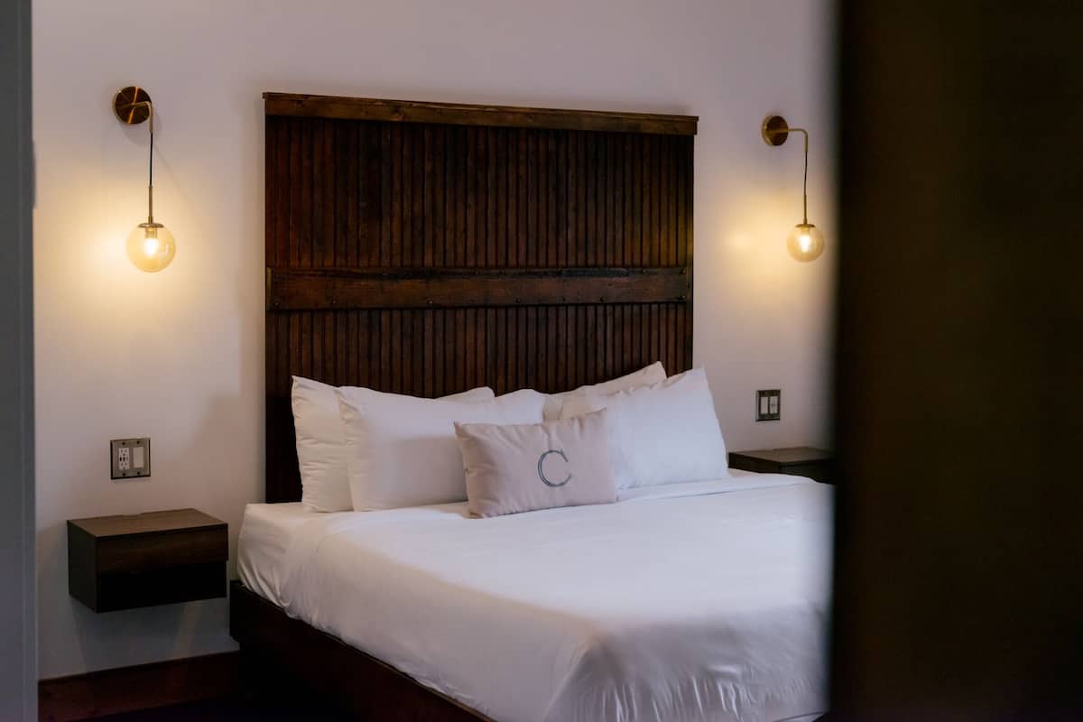 A neatly made bed with white linens and a wooden headboard, flanked by two bedside tables with wall-mounted lamps.