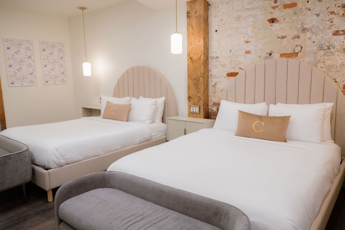 A hotel room with two beds, a small desk, and a bench.