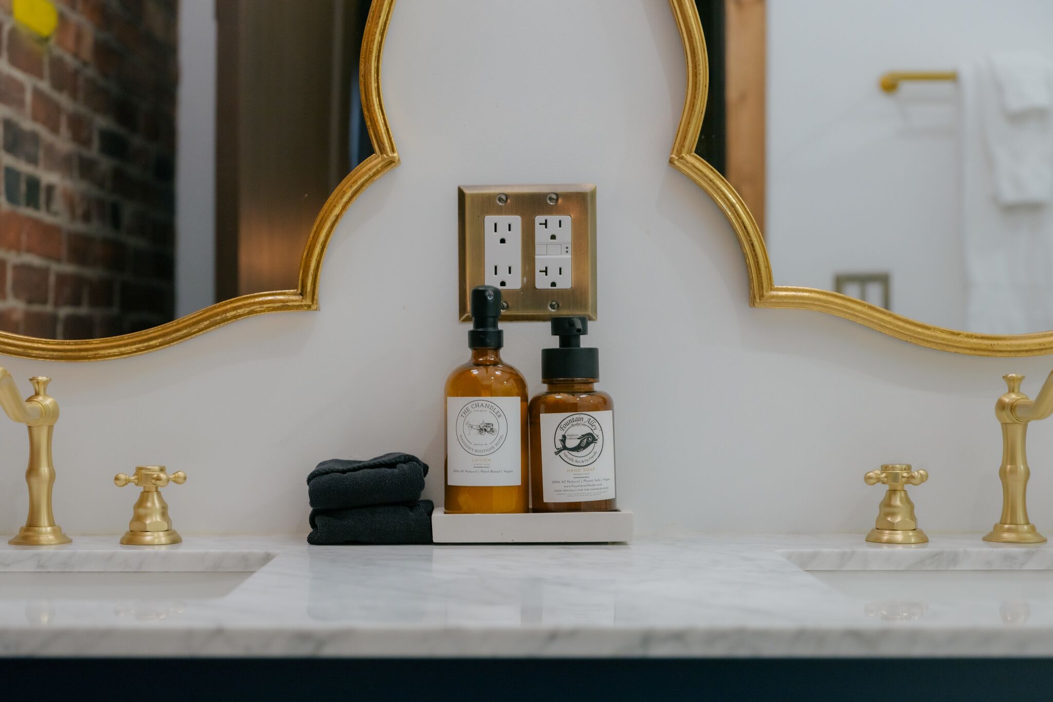 A bathroom vanity with a gold-framed mirror, two bottles of hand soap, and a black towel.