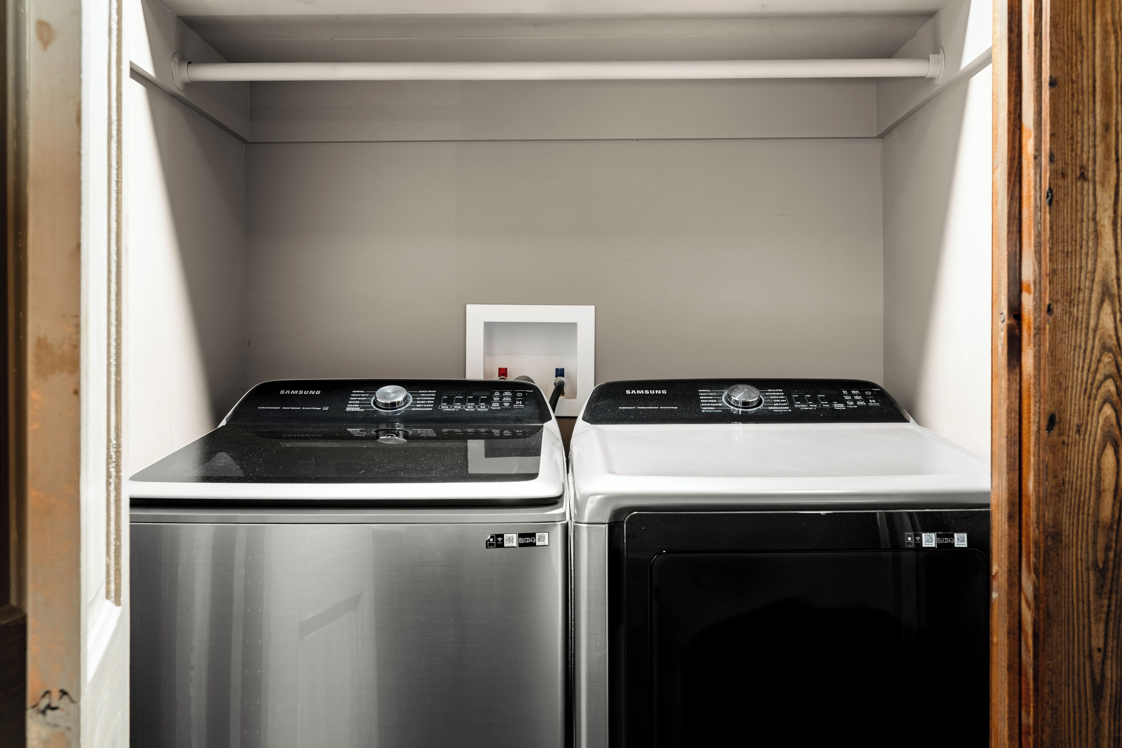 A laundry room with two stacked washers and dryers, a white door, and a wooden frame on the right.