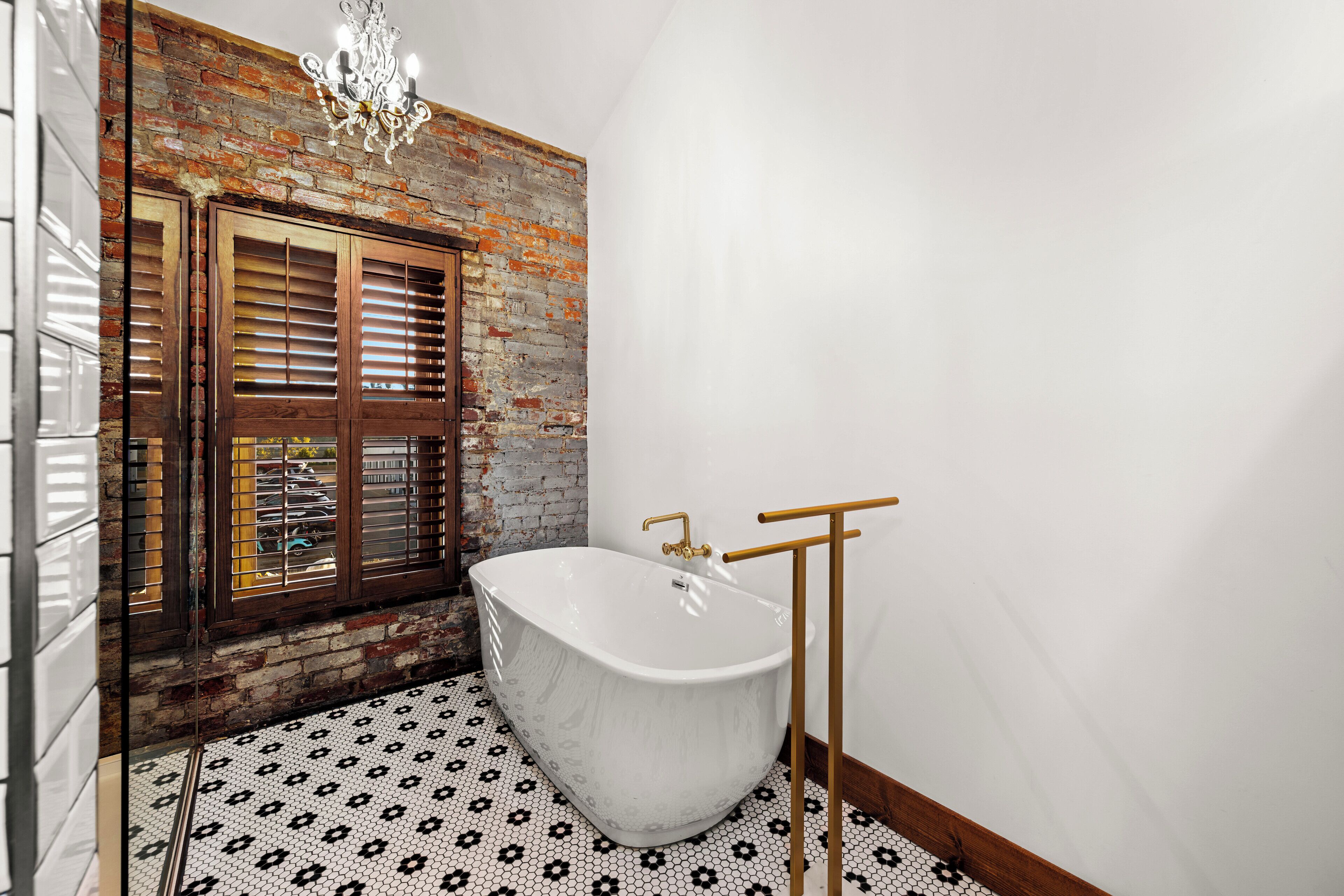 Un baño con una bañera independiente grande, una ventana de madera con persianas y un suelo estampado.