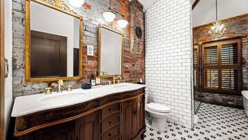 Un baño con pared de ladrillo rústica, piso de baldosas blancas y tocador de madera con dos lavamanos.