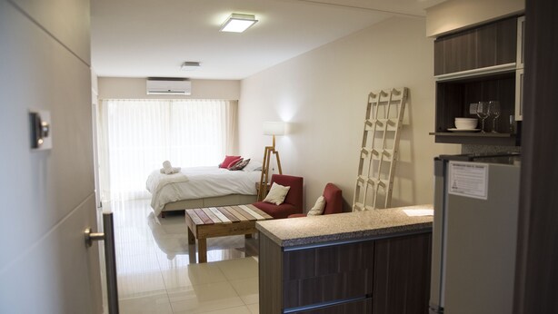 Een hotelkamer met een bed, een bureau, een stoel, een lamp, een koelkast en een raam met gordijnen.