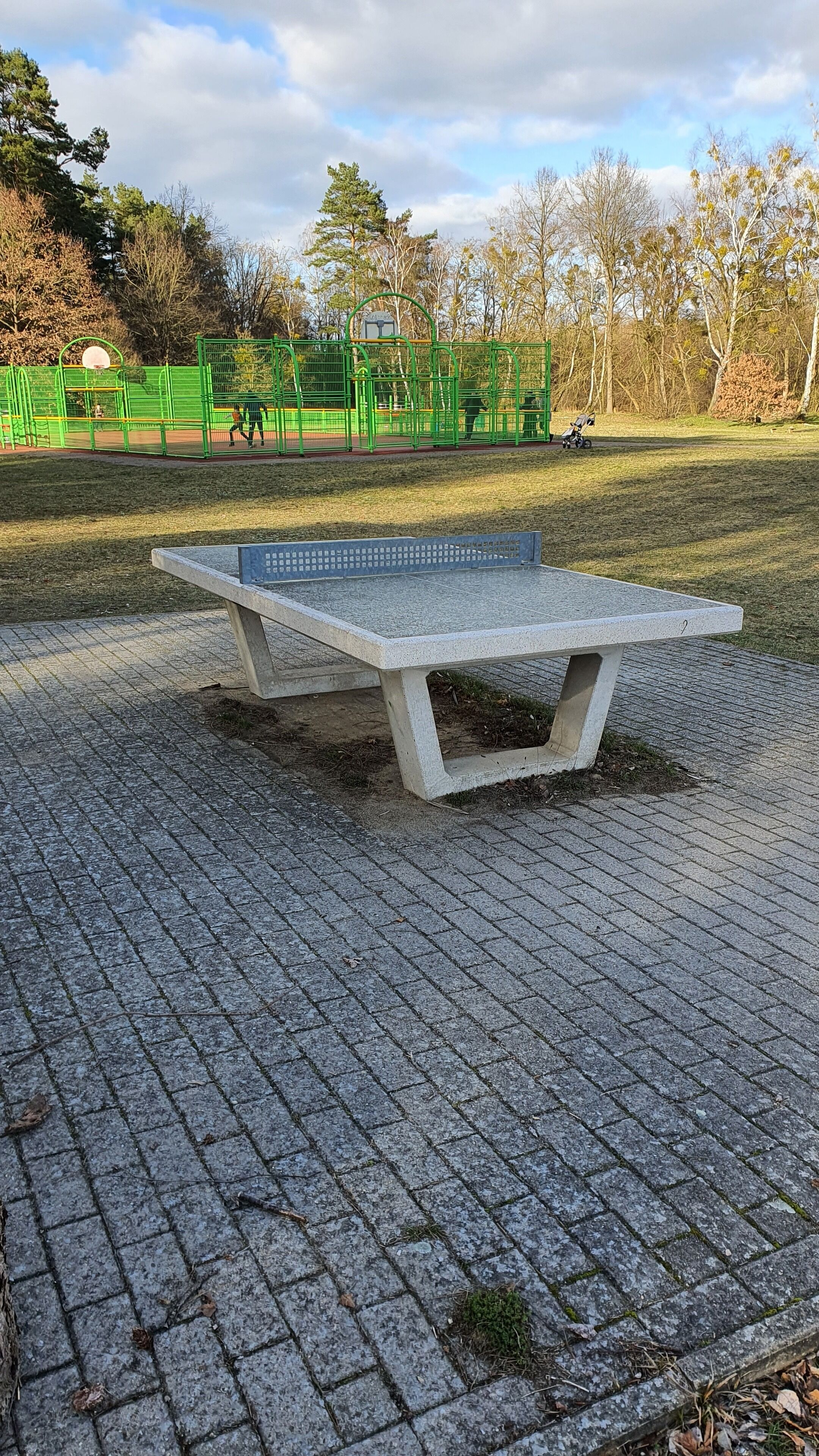 Betoninen penkki puistossa, taustalla leikkikenttä.