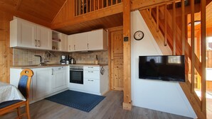 Een houten interieur met een keuken, een eethoek en een aan de muur bevestigde televisie.