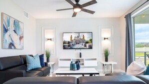 A modern living room with a black leather sofa, a white coffee table, and a flat-screen TV mounted on the wall.
