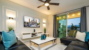 A modern living room with a flat-screen TV, a ceiling fan, and a large window with curtains.