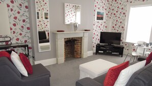 A living room with a fireplace, a television, and floral wallpaper. - Special seafront apartment with stunning view in characterful Victorian building (Portsmouth)