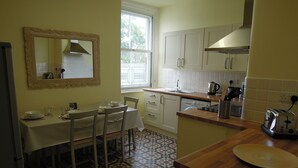 A kitchen with a dining table, chairs, a window, cabinets, and a countertop. - Special seafront apartment with stunning view in characterful Victorian building (Portsmouth)