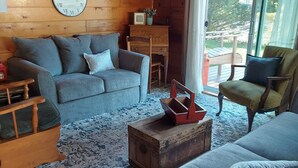 Ein gemütliches Blockhauss-Interieur mit Holzbalkendecke, großem Fenster, einer Couch, einem Fernseher und einer Wanduhr.